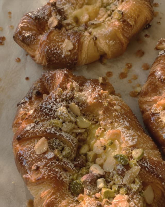 Viennoiseries dorées avec des éclats en garniture, posées sur une feuille de papier cuisson.